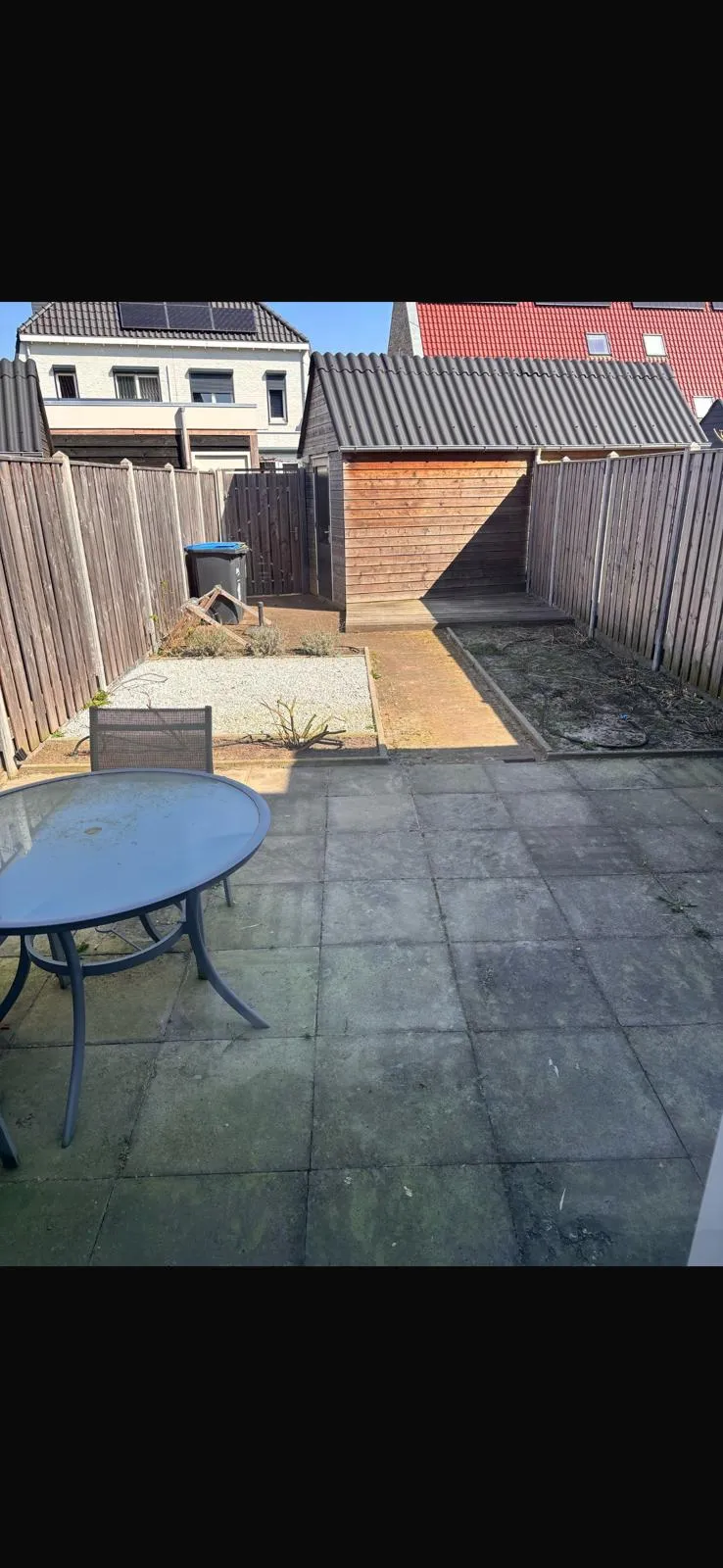 De tuin vóór de aanleg: veel tegels, kleine plantvakken en een schuur achterin