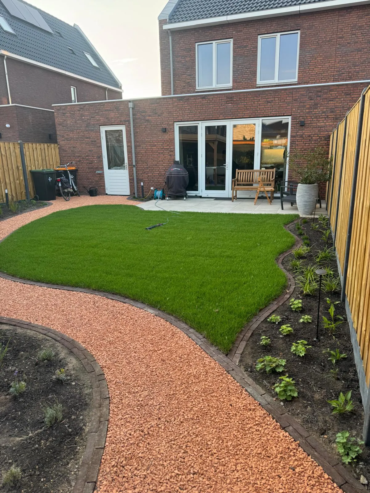 Een nieuw gazon met ronde vormen, een oranje grindpad en beplante borders