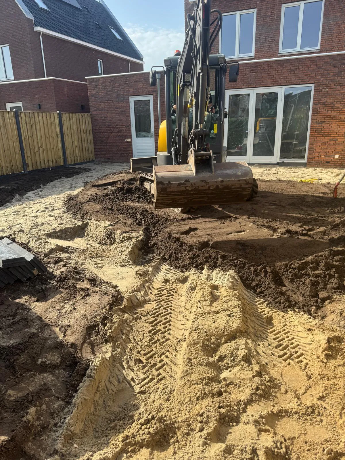 Minigraver verplaatst grond in een achtertuin bij een bakstenen woning