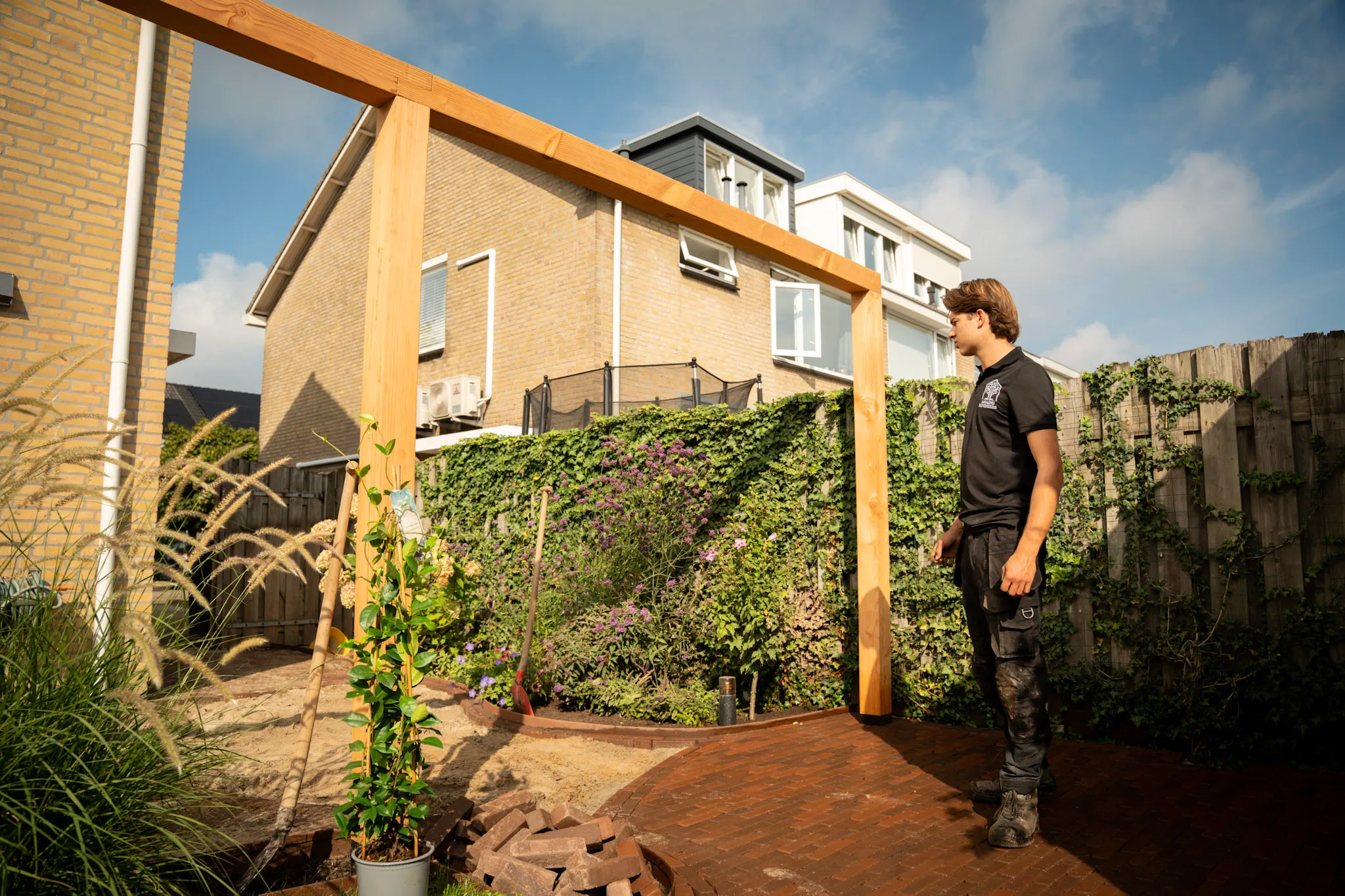 Jaap bij een houten pergola, bestrating en beplanting tijdens de aanleg