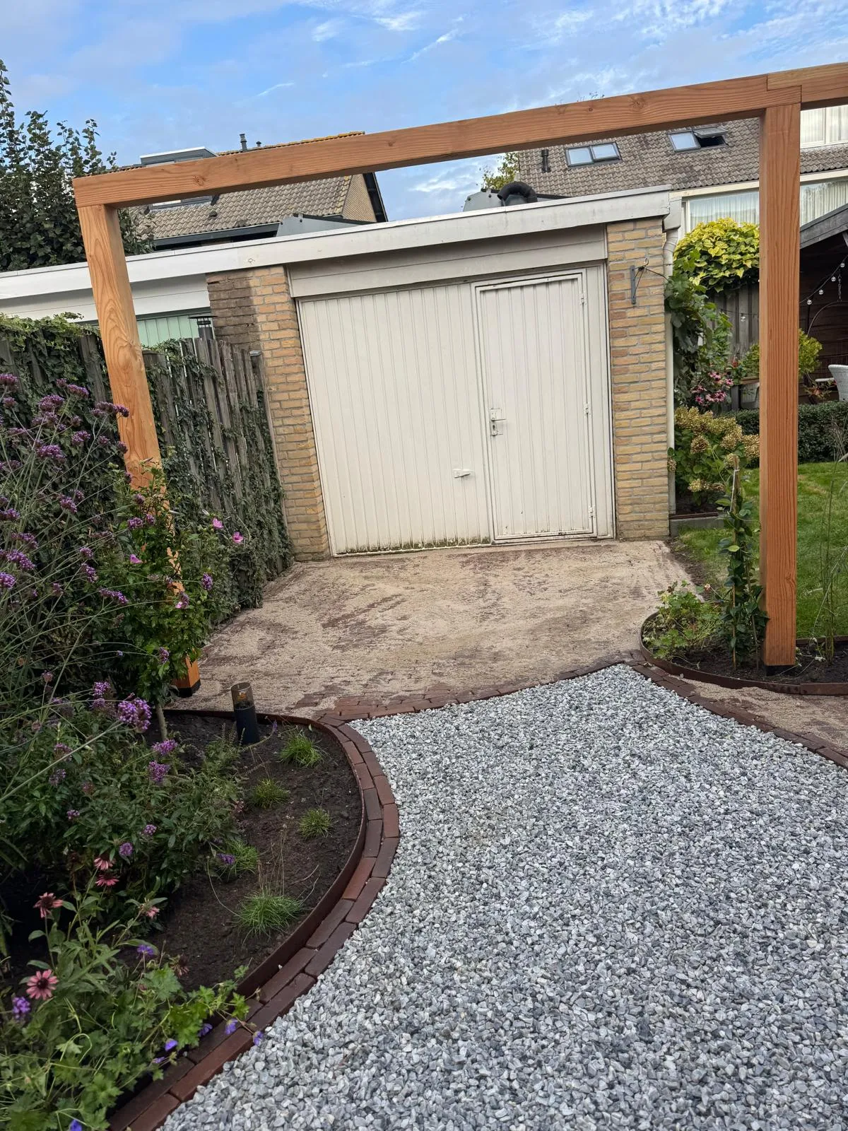 Pergola bij een garage, met een slingerend grindpad en beplanting