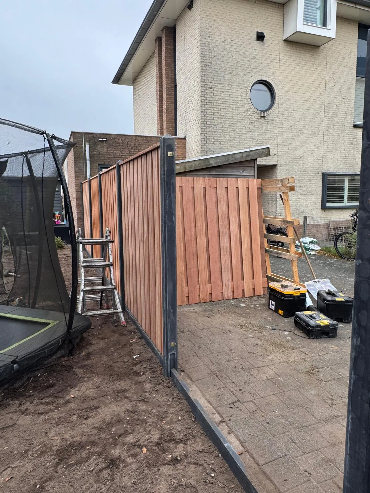 Een houten schutting met donkere palen wordt geplaatst, met gereedschap ernaast