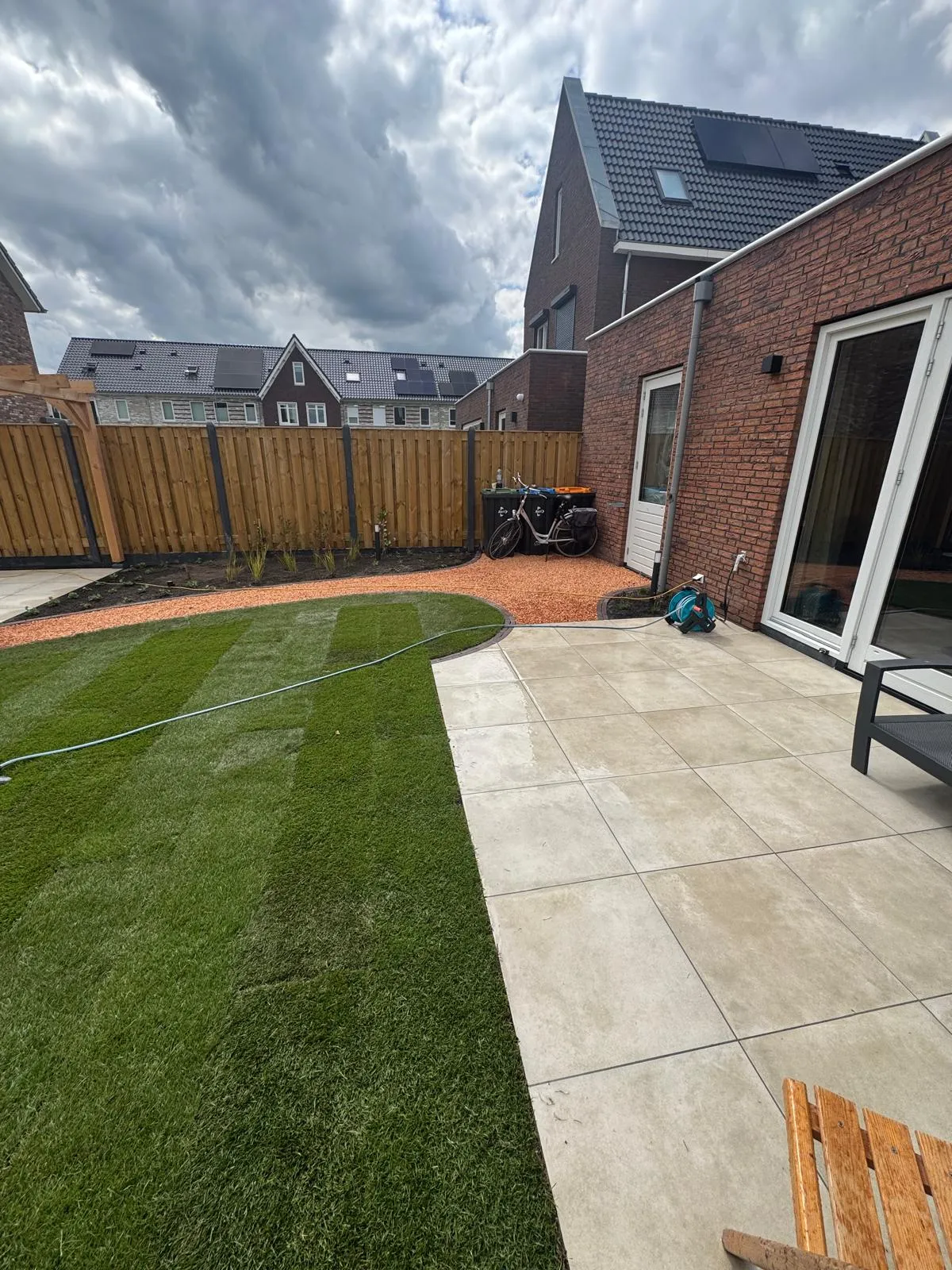 Licht betegeld terras naast een nieuw gazon en grindpad bij een woonhuis