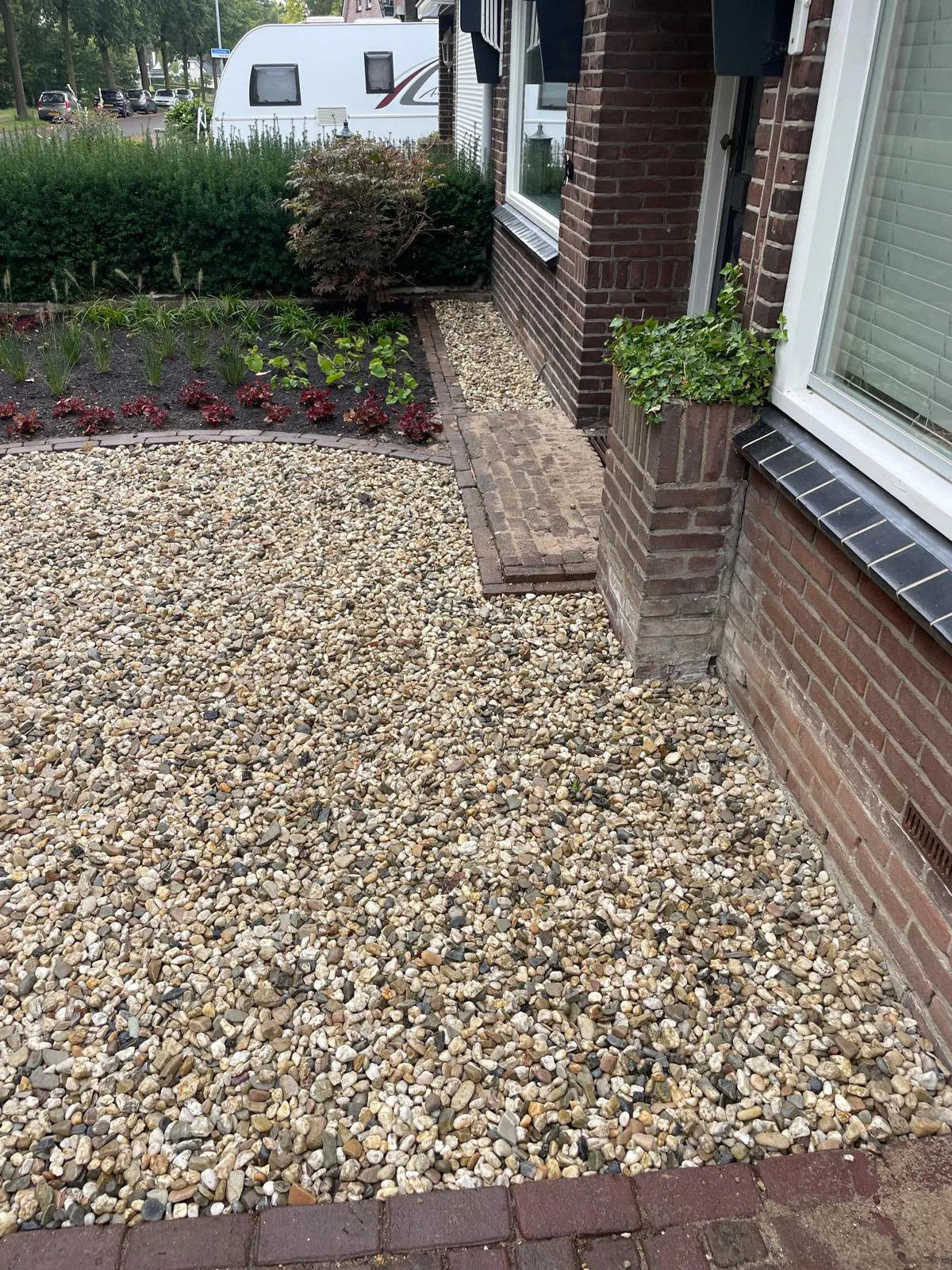 Grindvak en jonge planten naast de gevel, afgewerkt met een gebogen klinkerrand